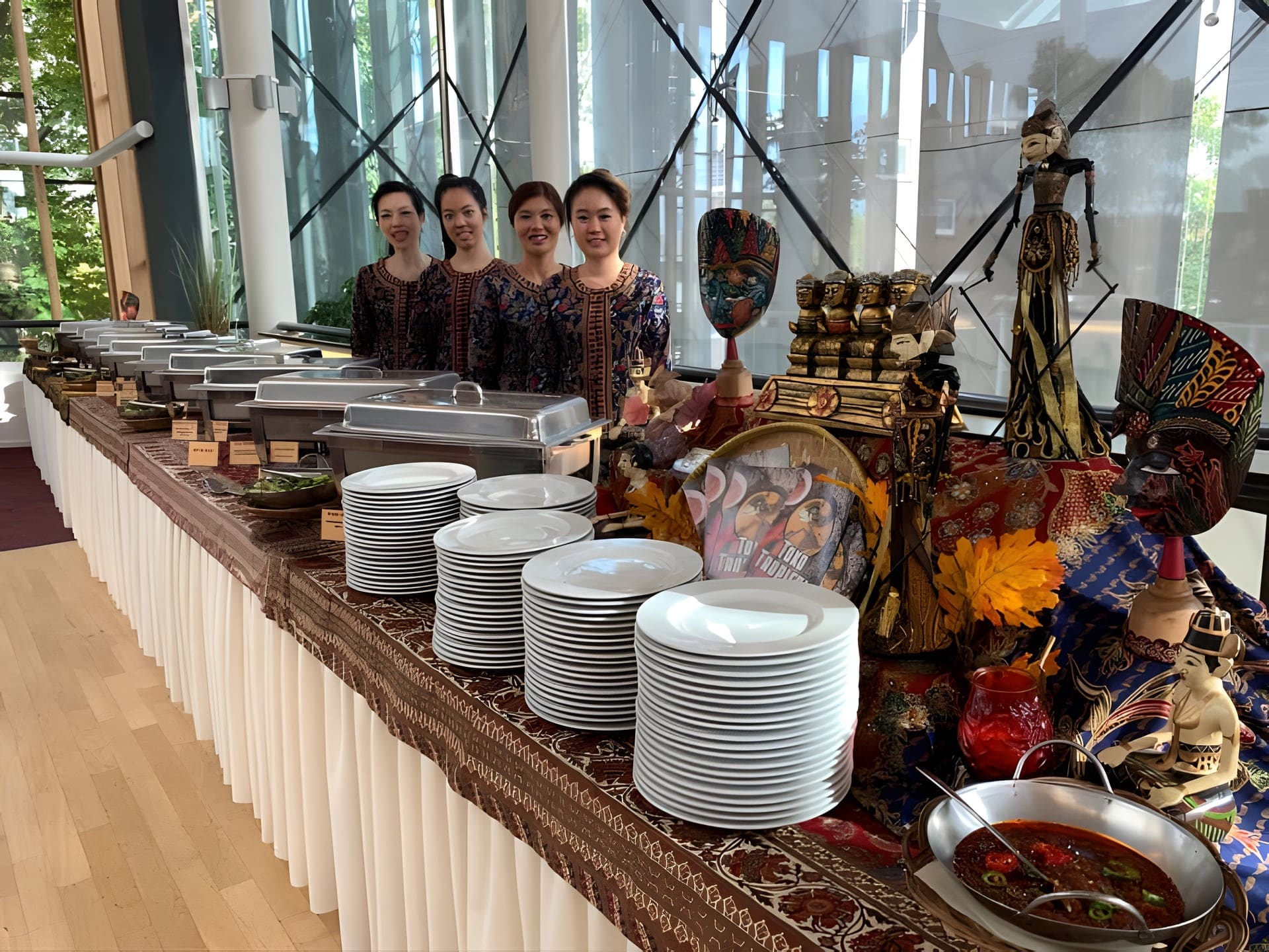 Het team van Toko Tropical in batikkleding achter het cateringbuffet, omringd door Indonesische wajangpoppen en maskers